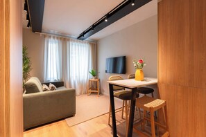 A modern living room with a sofa, a dining table with chairs, a TV mounted on the wall, and a potted plant. - 3 Comfy Houses by HostWise (Porto)