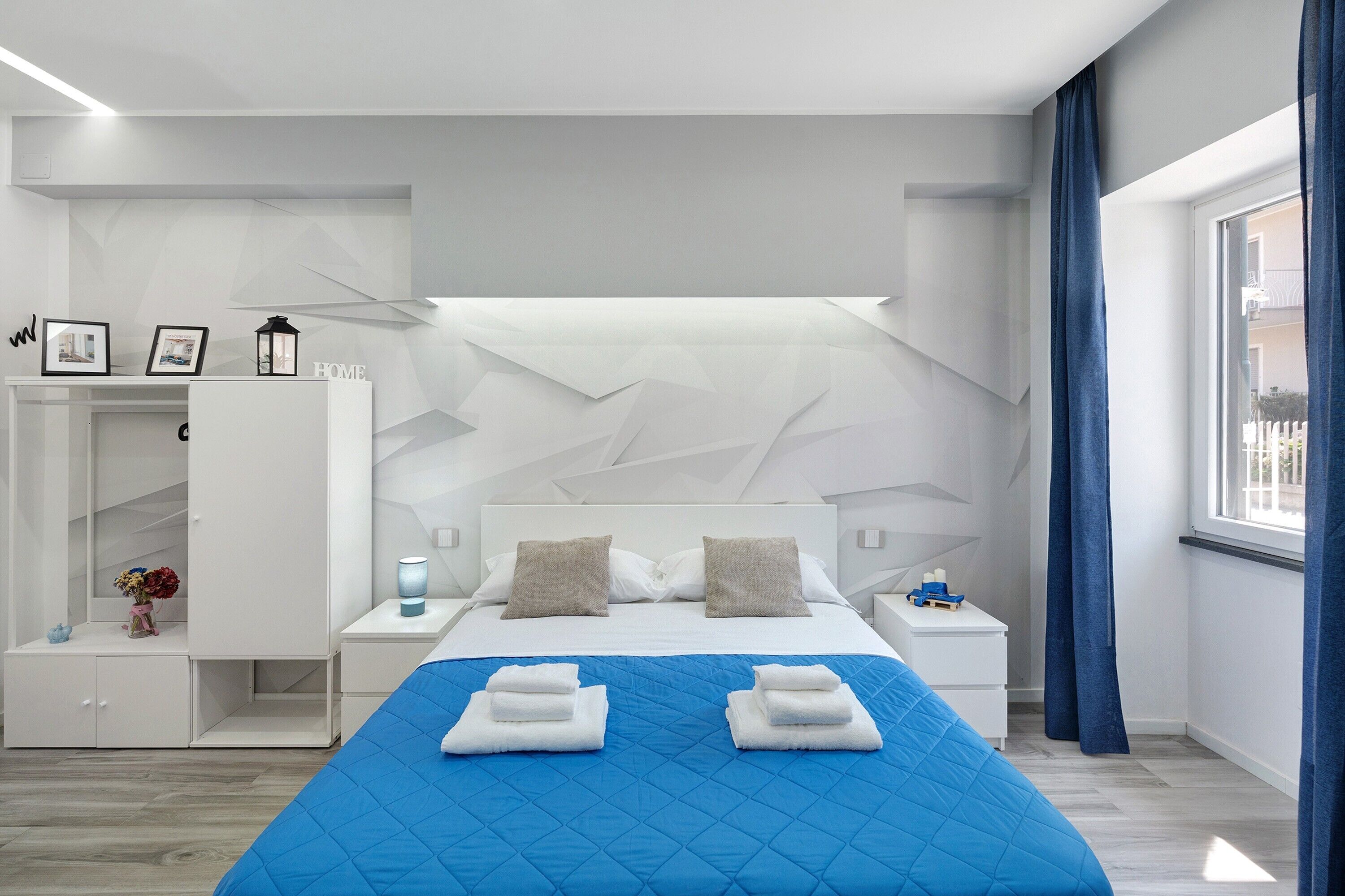 A modern hotel room with a large bed, a wardrobe, a nightstand, and a view of the outside.