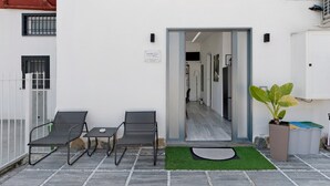 An outdoor seating area with two chairs and a table, a potted plant, and a door leading to an interior space.