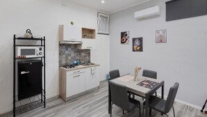 Une cuisine compacte équipée d’un four à micro-ondes, d’une cuisinière et d’un évier, ainsi qu’une table à manger avec des chaises et une petite fenêtre avec des rideaux.