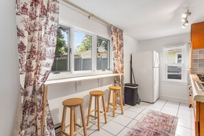 Une cuisine avec une fenêtre, trois tabourets en bois, une poubelle et un réfrigérateur.