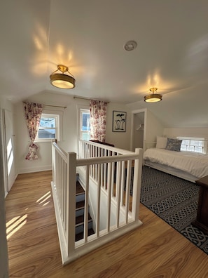 A bedroom with a bed, a staircase, and two windows with curtains. - The Darling Duplex South: Six guests. Three bedrooms. One full bathroom. (South Haven)