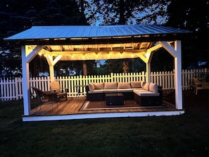 Ein überdachter Außenbereich mit weißen Holzzaun, Terrassendielen und Lichterketten.