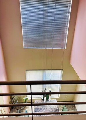 Ein Zimmer mit hohen Decken, einem Balkon mit Geländer und einem Fenster mit Jalousien.