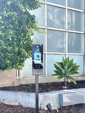 A parking meter with a digital display, a small succulent plant, and a building with large windows in the background. - Elegant, Stylish & Spacious Retreat / 3BD / 2.5 BA (Los Angeles)
