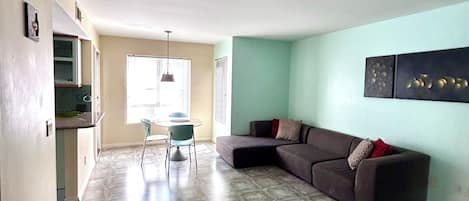 A living room with a sectional sofa, a dining table with chairs, and a kitchen area.