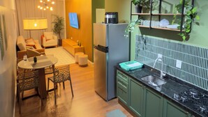 A modern kitchen with a refrigerator, stove, and green cabinets. There is a dining area with a table and chairs, and a TV mounted on the wall. - Zoe  (Foz do Iguaçu)