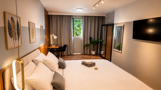 A modern hotel room with a large bed, a desk, a chair, a TV, and a window with curtains. - Zoe  (Foz do Iguaçu)