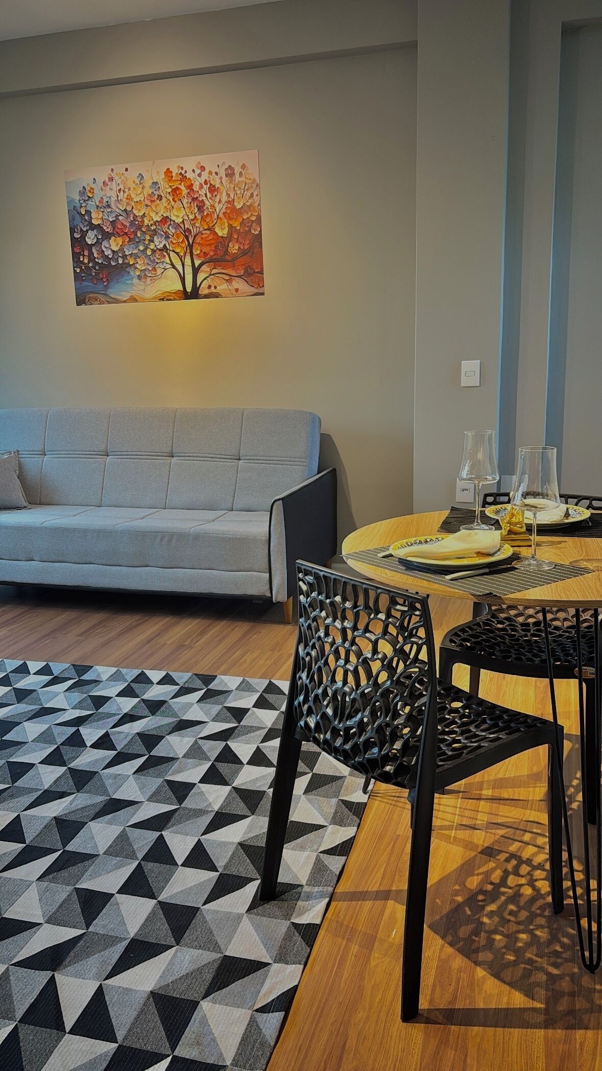 A modern living room with a sofa, dining table, chairs, a geometric rug, and a wall-mounted painting.