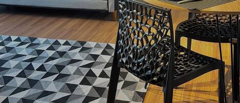 A modern living room with a sofa, dining table, chairs, a geometric rug, and a wall-mounted painting.