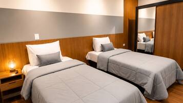 Quarto de hotel com duas camas, cabeceiras de madeira, uma mesa de cabeceira com abajur e um espelho grande.