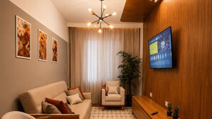 A modern living room with a sofa, armchair, and a television mounted on the wall. - Zoe  (Foz do Iguaçu)