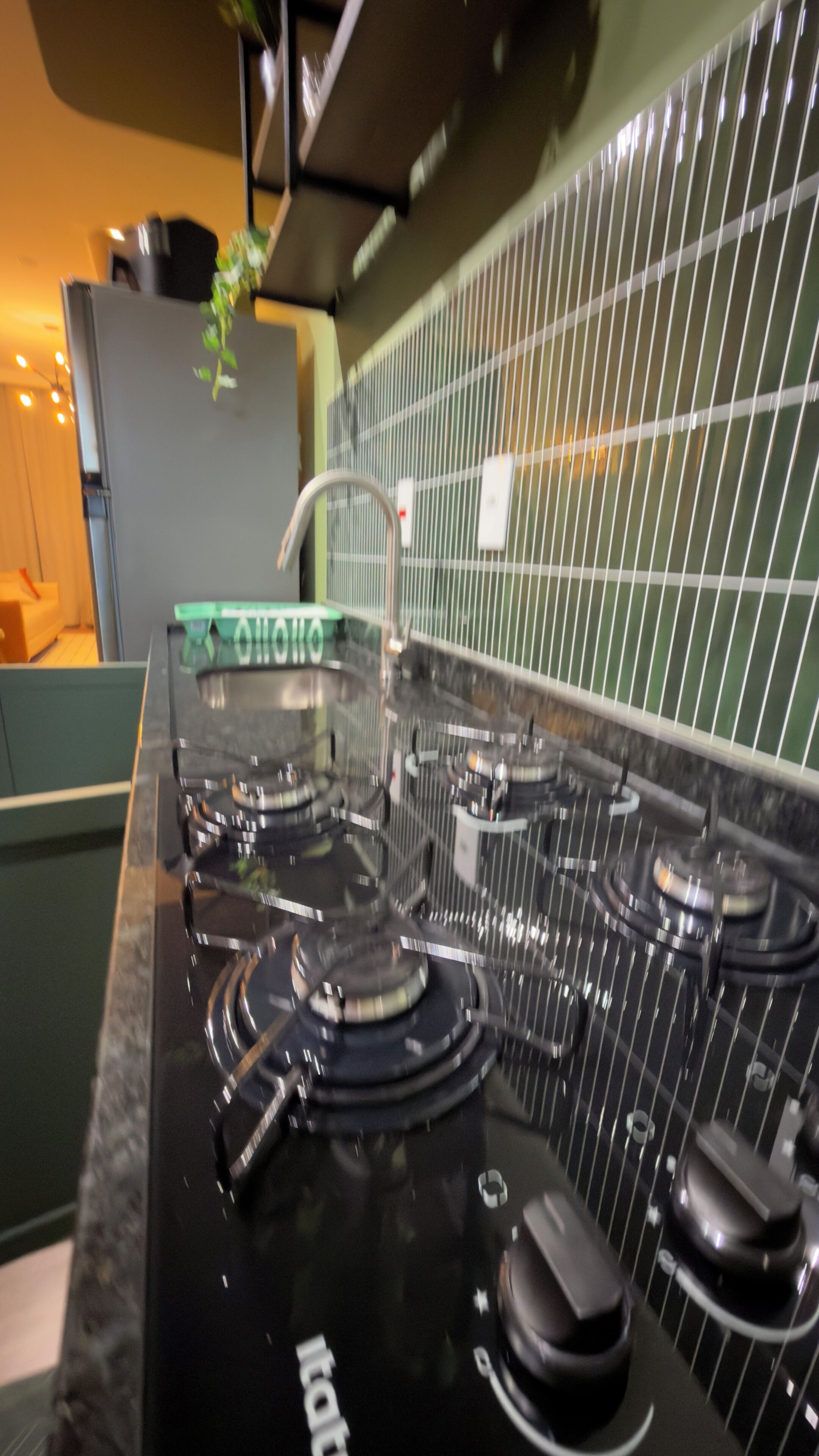 Uma cozinha com fogão preto, painel verde e parede revestida de azulejos brancos.