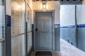 Uma porta cinzenta com fechadura eletrônica, uma pequena placa iluminada acima dela e o número '301' na parede.