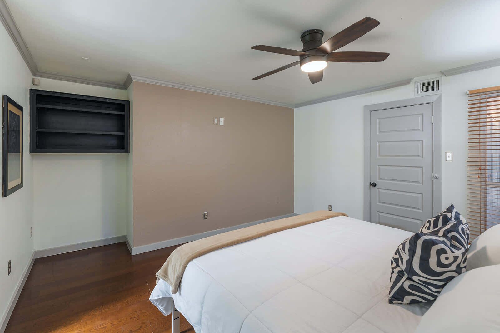 A bedroom with a bed, a ceiling fan, a door, and a window with blinds.