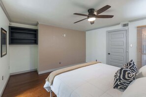 Un dormitorio con cama, ventilador de techo, puerta y ventana con persianas.
