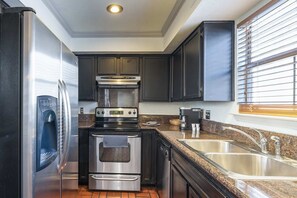 A compact kitchen with a refrigerator, oven, dishwasher, and a double sink. - Spacious Austin Retreat 3BR Pool Views (Austin)