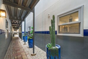 Corredor com vasos de plantas, uma janela com persianas e estrutura de teto metálica.