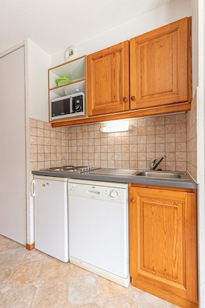 A compact kitchen with wooden cabinets, a built-in microwave, a dishwasher, and a tiled backsplash. - 1st floor, balcony, tv, ski locker, 35m², Aussois (Aussois)