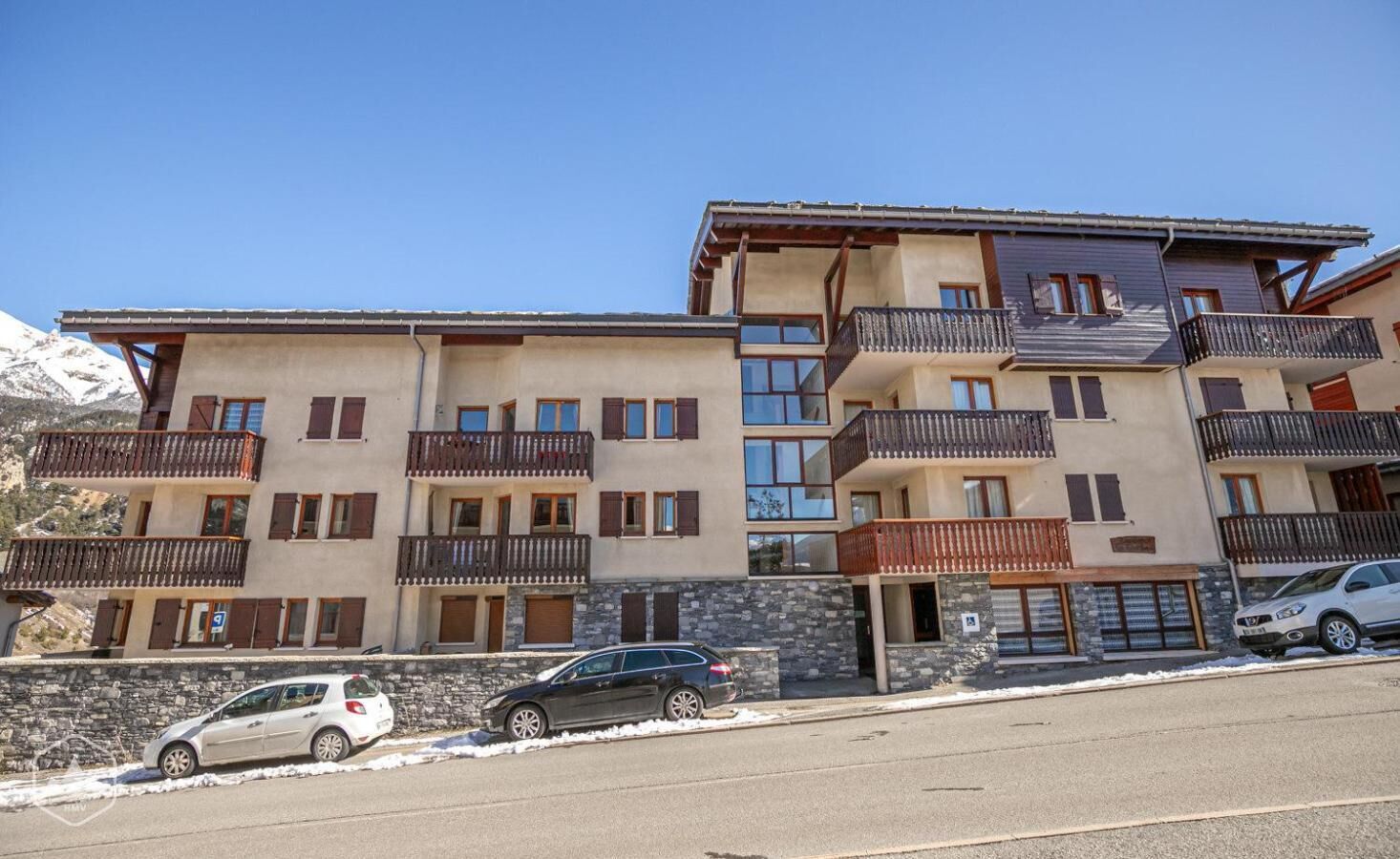A multi-story hotel with balconies, a stone facade, and a parking area.