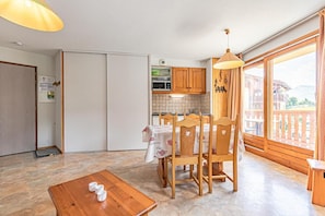 A kitchen with wooden cabinets, a dining table with chairs, a coffee table, and a large window with a view. - 1st floor, balcony, tv, ski locker, 35m², Aussois (Aussois)