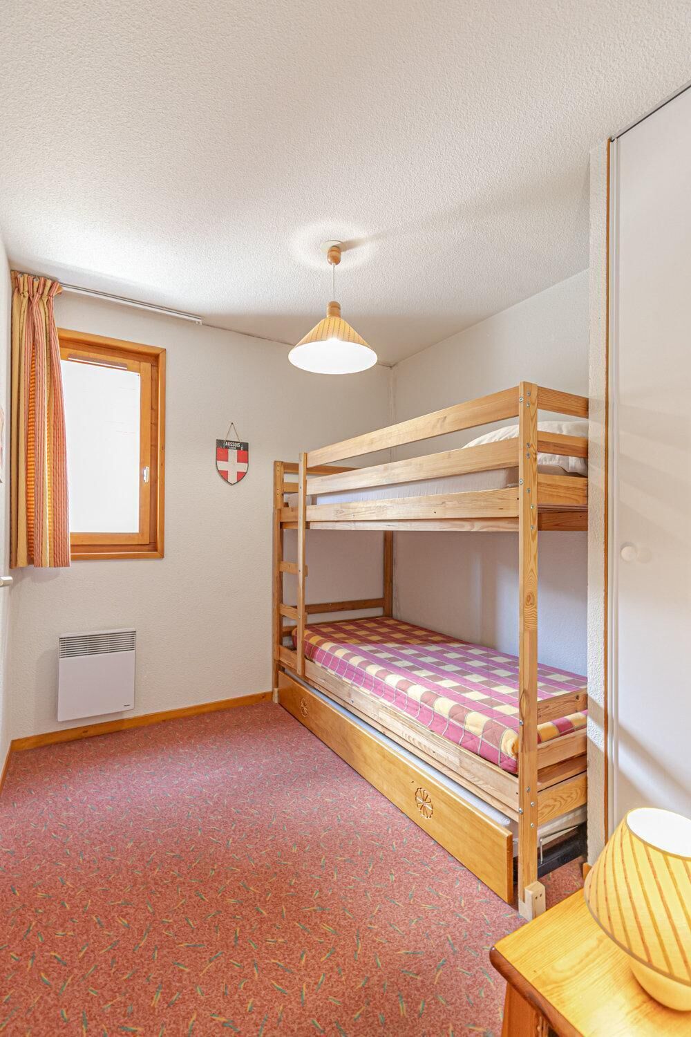 Een slaapkamer met een stapelbed, een raam, een radiator en een lamp op een tafel.