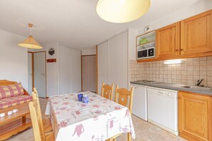 A compact kitchen with wooden cabinets, a microwave, a dishwasher, and a dining table with chairs. - 1st floor, balcony, tv, ski locker, 35m², Aussois (Aussois)