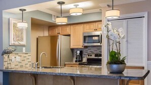 Une cuisine moderne dotée d’un îlot central, d’appareils électroménagers en acier inoxydable et de luminaires suspendus.