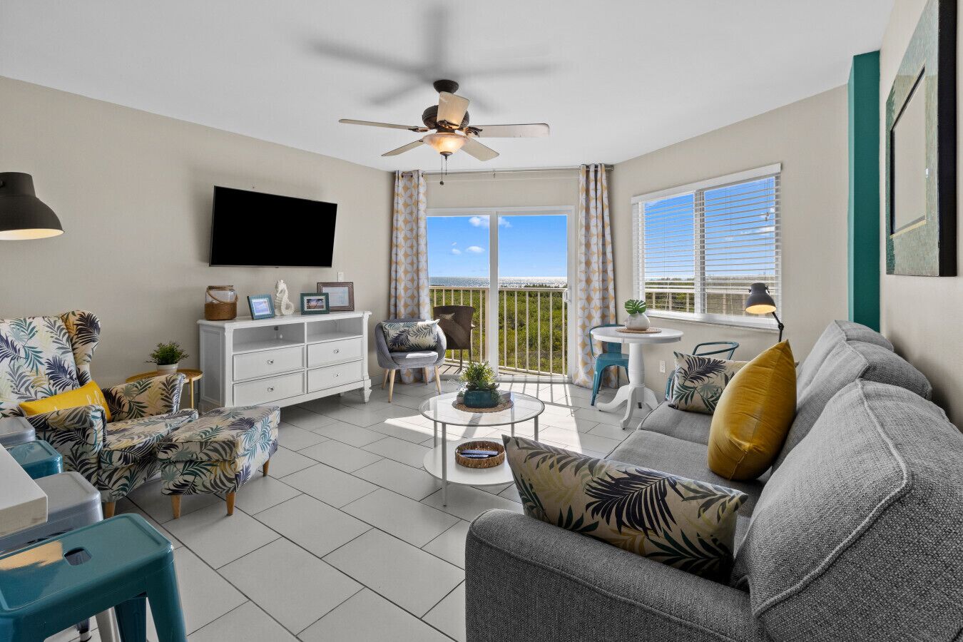 A living room with a ceiling fan, a flat-screen TV, a sofa, a coffee table, and a balcony with a view.