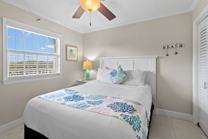 A bedroom with a bed, a ceiling fan, a nightstand with a lamp, a window with blinds, and a wall with the word 'BEACH' spelled out. - Exceptional OceanView 2/2 heated Pool Beach Marina (Tavernier)