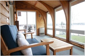 Uma cabana de madeira com área de estar, incluindo um sofá e uma mesa, janelas amplas e vista para o exterior.