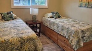 A bedroom with two single beds, a nightstand, a lamp, and a painting on the wall. - Serene Hauula Retreat with Ocean Views (Hauula)