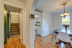 Ein Essbereich mit einem runden Tisch, Stühlen und einer Deckenleuchte. Im Hintergrund ist eine Treppe zu einem anderen Raum sichtbar.