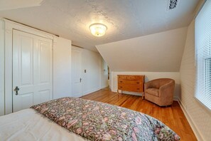 Une chambre à coucher avec un lit, une commode, une chaise et une fenêtre avec des stores.