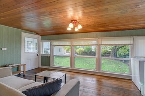 Ein Zimmer mit Holzboden, einer Couch, einem Couchtisch und großen Fenstern mit Blick auf einen Garten.