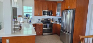A modern kitchen with wooden cabinets, stainless steel appliances, and a white countertop. - Islamorada Gem / 5BR Oceanfront Home w/ Stunning Ocean Views (Tavernier)