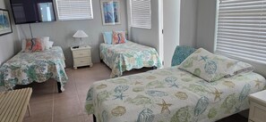 A bedroom with two single beds, a nightstand, a TV, and a window with blinds. - Islamorada Gem / 5BR Oceanfront Home w/ Stunning Ocean Views (Tavernier)