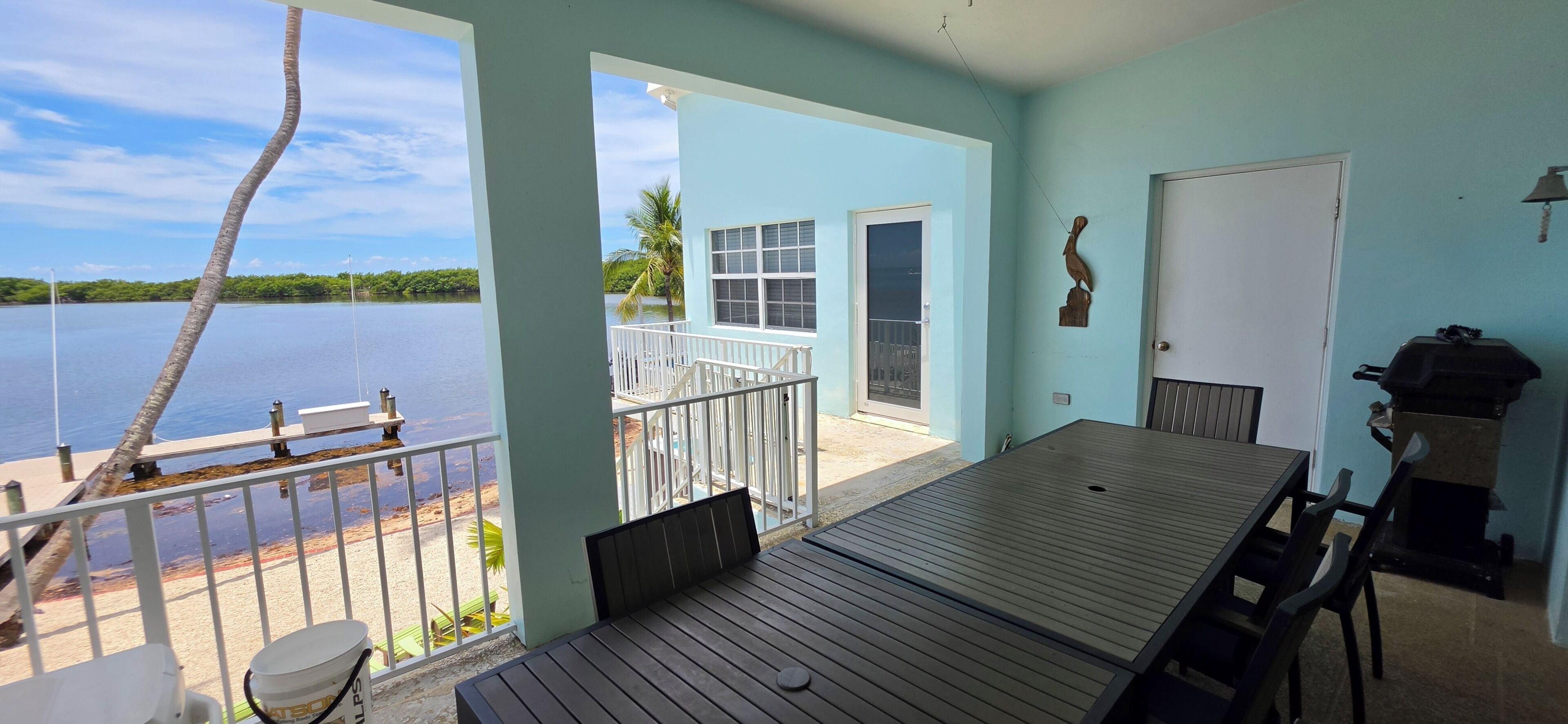 A balcony with a view of a lake, a table, chairs, a grill, and a door.