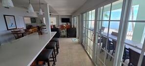 A spacious kitchen with a long counter, dining area, and large sliding glass doors leading to a balcony with outdoor furniture. - Islamorada Gem / 5BR Oceanfront Home w/ Stunning Ocean Views (Tavernier)