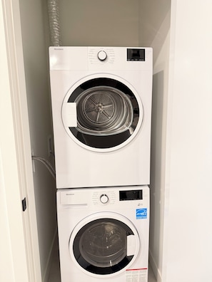 A wall-mounted, stacked washer and dryer unit with a control panel and a digital display. - Modern Condo Steps From SkyTrain-Walkable Location + Amazing Building Amenities (Surrey)