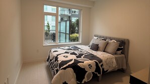 A bedroom with a bed, a window, and a ceiling light. - Modern Condo Steps From SkyTrain-Walkable Location + Amazing Building Amenities (Surrey)
