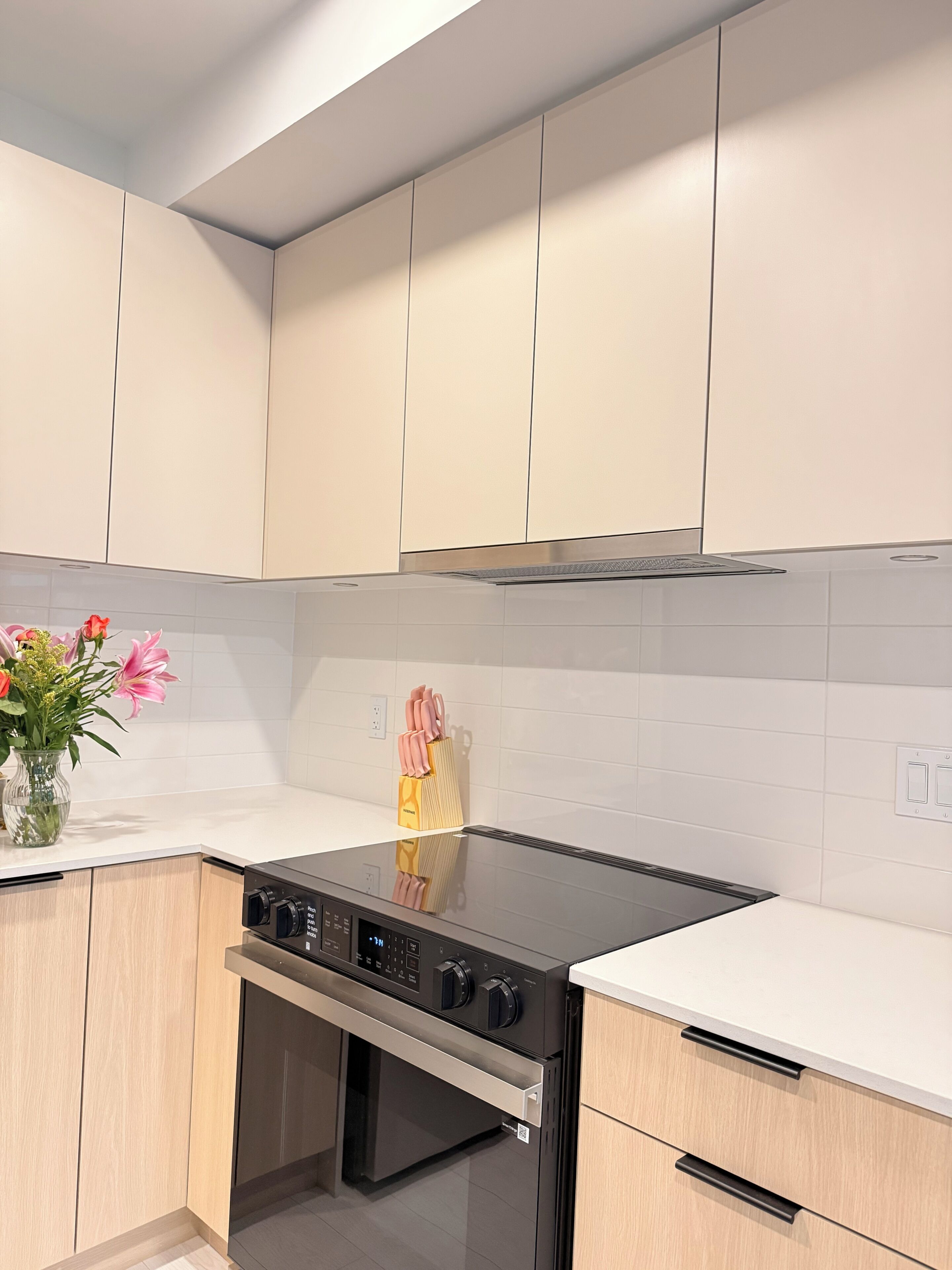A kitchen with a black stove, wooden cabinets, and a white tiled backsplash.