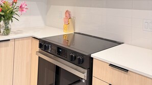 A kitchen with a black stove, wooden cabinets, and a white tiled backsplash. - Modern Condo Steps From SkyTrain-Walkable Location + Amazing Building Amenities (Surrey)