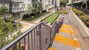 A multi-story residential building with balconies, a central courtyard with a lawn, and a staircase with yellow safety markings. - Modern Condo Steps From SkyTrain-Walkable Location + Amazing Building Amenities (Surrey)