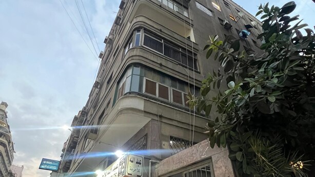 Un immeuble à plusieurs étages, avec un commerce au rez-de-chaussée, une entrée sécurisée par un portail et une enseigne visible indiquant le nom de l’entreprise.