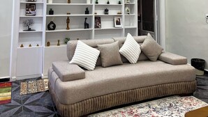 Un salon moderne avec un canapé, une étagère blanche remplie d’objets décoratifs et un tapis à motifs.