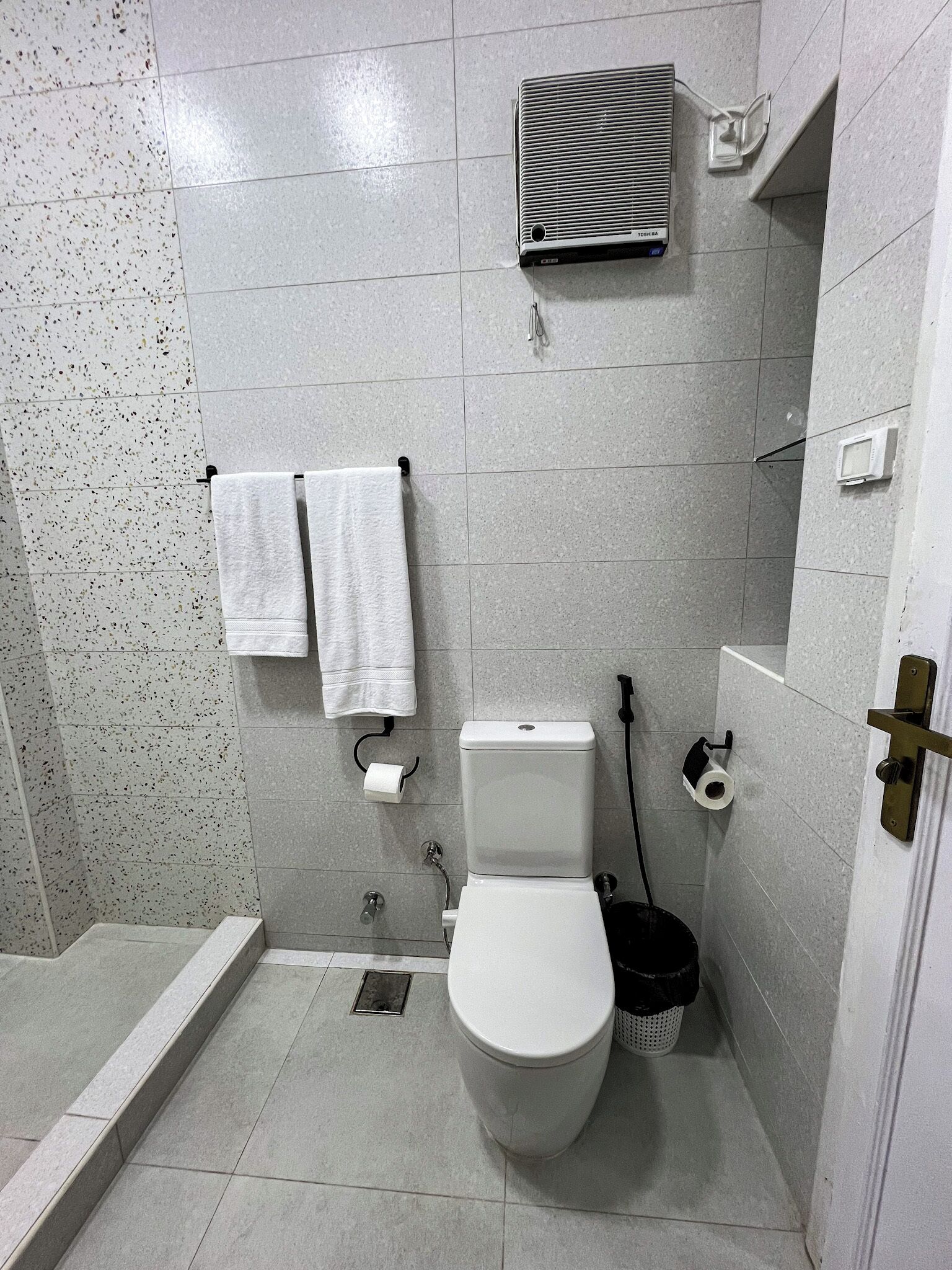 A small, modern bathroom with a toilet, two white towels, a shower, and a toilet paper holder.