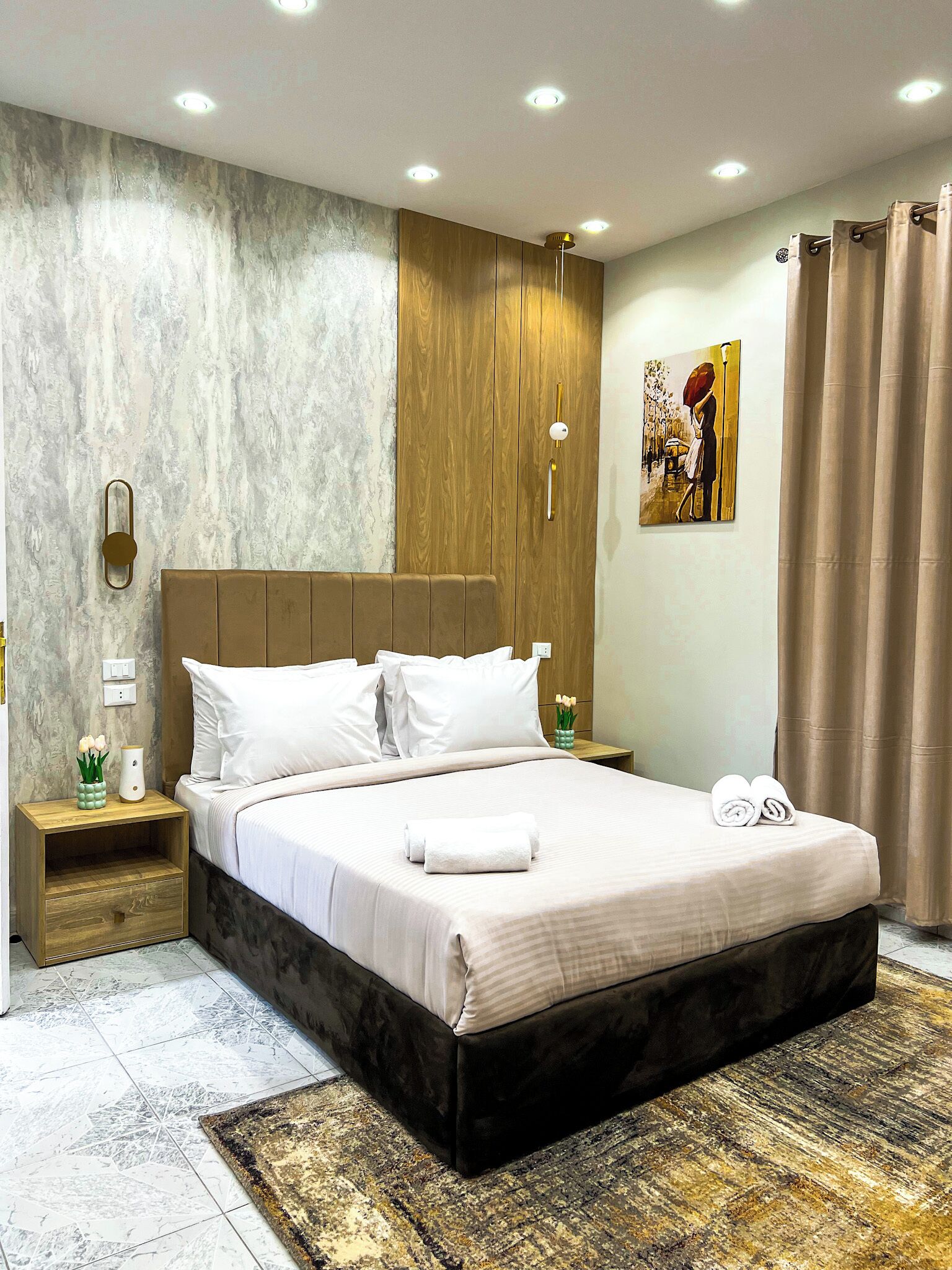 Un dormitorio moderno con una cama grande, cabecera de madera y pared con estampado de mármol.
