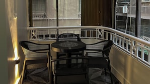 Un balcon d’angle avec une table ronde et quatre chaises, de grandes fenêtres et un sol à motifs.