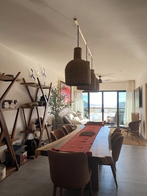 A dining area with a long table, chairs, hanging wicker lamps, and a view of the outdoors through large windows. - 2-bedroom Seaview  penthouse apartment in peaceful Cabo San Lucas with AC (Cabo San Lucas)
